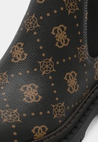 Gros plan d'une chaussure en cuir noir avec des motifs géométriques et un logo écrit couleur fauve répétitifs et une bordure de semelle cousue.