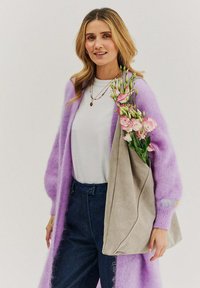 Svetlofialový kardigán s dlhými rukávmi cez biele tričko. Sivá taška nesie ružové kvety. Modré rifľové nohavice so zapínaním na gombíky.