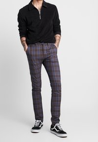 Svart zip-up pullover i mjuk tyg, kombinerad med rutiga byxor i blått, lila och kräm, kompletterad med svart och vit sneakers.