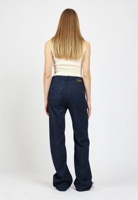 Dunkelblaue Denim-Jeans mit ausgestelltem Bein, mittlerer Taille und Fünf-Taschen-Design. Auf der Rückseite befindet sich ein Markenetikett und dezente Zierstiche.