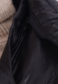 Interno di una giacca a vento nera con una texture liscia e lucida e cerniera visibile. Adiacente c'è un tessuto lavorato a maglia di un beige chiaro.