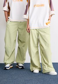 Lichtgroene, losse broek gemaakt van lichtgewicht stof; gedragen met oversized witte truien met kleurrijke accenten en logo's.