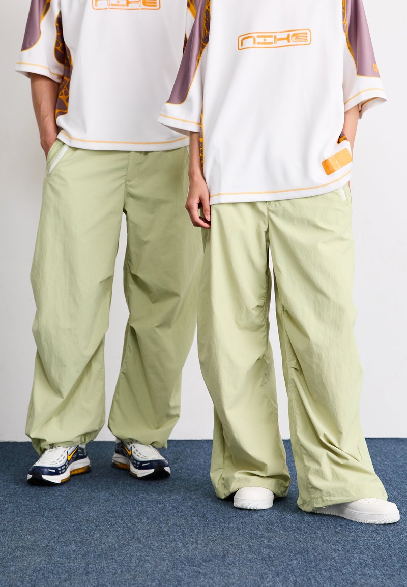 Pantaloni verde chiaro, a vestibilità ampia, realizzati in tessuto leggero; indossati con maglie bianche oversize con accenti e loghi colorati.