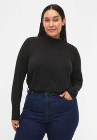 Musta pitkähihaisen paita korkealla kauluksella, valmistettu sileästä materiaalista, yhdistetty korkeavyötäröisiin sinisiin farkkuihin, joissa on taskut ja tavanomainen nappikiinnitys.