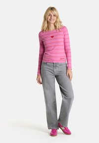 Rosa Langarmshirt mit horizontalen Streifen und kleinem roten Herzdetail, kombiniert mit hellgrauen weit geschnittenen Jeans und rosa Turnschuhen.