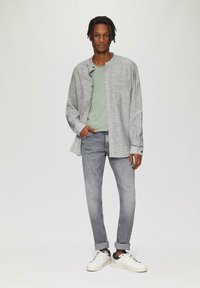 Lichtgrijze geblokte overhemden, groene t-shirt, grijze slim fit jeans en witte sneakers met zwarte accenten. Casual outfit met gestructureerde pasvorm.