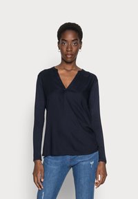 Haut à manches longues bleu marine avec un décolleté en V et une texture douce, associé à un jean en denim bleu, affichant une coupe décontractée et un design minimal.