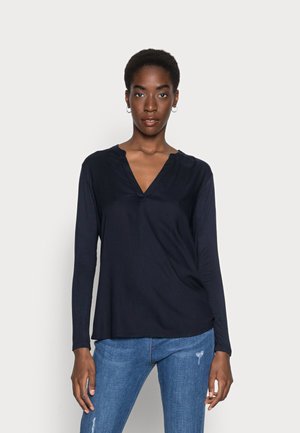 Haut à manches longues bleu marine avec un décolleté en V et une texture douce, associé à un jean en denim bleu, affichant une coupe décontractée et un design minimal.