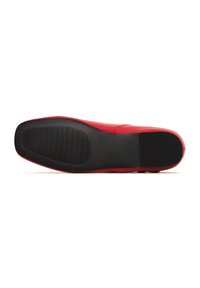 Roter Lederschuh mit einer flachen schwarzen Gummisohle, die eine glatte Oberfläche und eine subtile gerippte Textur auf der Sohle für besseren Halt aufweist.