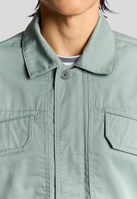 Groen lichtgewicht button-up jack met een kraag, twee borstzakken en duurzame stof met zichtbare stiksels.