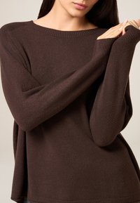 Brązowy sweter dziany z miękkiego materiału, o luźnym fasonie, szerokim dekolcie i długich rękawach z ściągaczami.