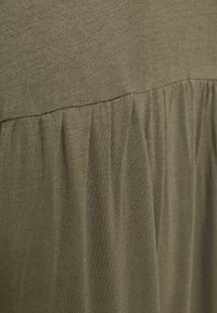 Oliwkowa sukienka z gładką górną częścią i marszczeniami na dole, wykonana z miękkiej, lekkiej tkaniny.