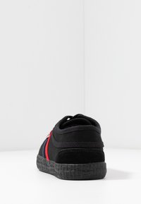 Black sneaker with textured rubber sole, featuring red and blue stripes. Constructed from canvas, with a padded collar for comfort.