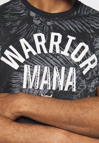 Černé grafické tričko s nápisy "WARRIOR" a "MANA" v tučném bílém písmu. Design zahrnuje jemné texturované vzory na látce.