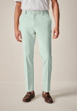 Pantalones de tiro alto en verde menta claro, con corte entallado, que presentan un cierre de un solo botón y bolsillos laterales, combinados con mocasines marrones.