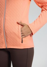 Lichte, gestructureerde koraalkleurige jas met een ritszak, contrasterende gladde rugpaneel en aansluitende mouwen, gecombineerd met brown leggings.