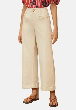 Beežid laiade säärtega püksid punutud taskute detailidega, nööbitud vöökohaga, koos punaste rihmikandadega ja punase mustrilise särgiga.