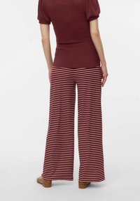 Haut côtelé bordeaux associé à un pantalon large à rayures bordeaux et crème. Texture lisse, coupe décontractée et manches légèrement bouffantes.