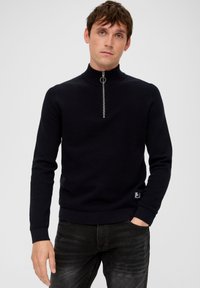 Granatowy sweter dzianinowy z wysokim kołnierzem i zamkiem błyskawicznym do połowy, z prążkowanymi mankietami i dołem oraz małą metką z logo na dole.