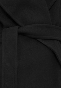 Roupa de casa preta em fleece com um design envolvente, apresentando um cinto de tecido e uma textura suave e macia. Sem padrões visíveis ou detalhes de metal.