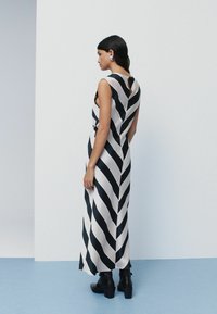 Vestido maxi de satén a rayas blancas y negras con espalda con abertura, diseño sin mangas y combinado con botas negras hasta el tobillo. Textura suave.