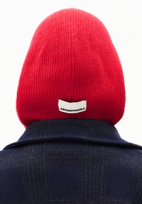 Rote gerippte Mütze mit einem Etikett "ARMEDANGELS" über einer nav-blauen gemusterten Jacke mit Kragen, die Textur und kontrastierende Farben betont.