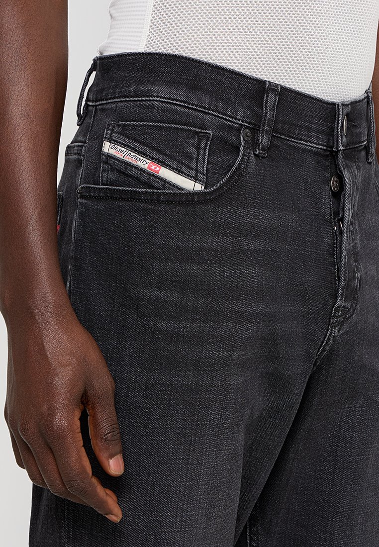 Jean en denim noir avec une coupe classique, présentant une poche avant avec une étiquette blanche visible et un design épuré. Le tissu a une légère texture.