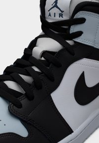 Πανύψηλα αθλητικά παπούτσια με συνδυασμό από μαύρο, λευκό και ανοιχτό μπλε δέρμα. Διαθέτουν υφές στην επιφάνεια, μαύρα κορδόνια και λογότυπο στη γλώσσα.