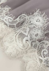 White floral lace fabric with intricate patterns and fine mesh over a soft gray background.