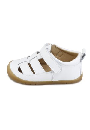 Sandalia blanca para niño pequeño con tres tiras, cierre de velcro ajustable, suela marrón claro y diseño de punta abierta sobre fondo blanco.