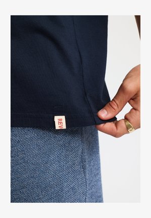 Middendonkblauw katoenen t-shirt met een rechte zoom en een label opzij. De stof lijkt zacht, heeft een gladde textuur en minimale details.