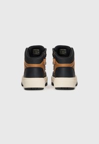 Chaussures mi-hautes noires et brunes avec une tige en cuir texturé, semelle en caoutchouc crème et zips latéraux pour un enfilage facile.