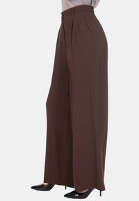 Pantaloni marroni a gamba larga con pieghe frontali, vita alta e tessuto liscio. Abbinati a tacchi neri a punta per un look complessivo migliorato.