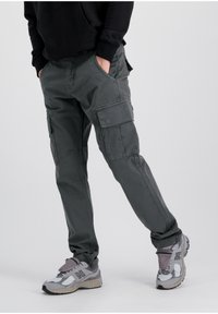 Pantalones cargo de tela gris oscuro con múltiples bolsillos y un corte relajado. Combinados con zapatillas deportivas grises y plateadas. Textura suave.