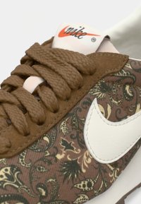Bruine sneakers met een paisleypatroon stof, crème leren accenten en dikke bruin veters. Nike-logo prominent op de tong.