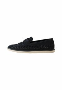 Mocasines de ante negro con detalles trenzados, suela plana beige y una forma elegante. Presenta una correa en el empeine para un estilo adicional.