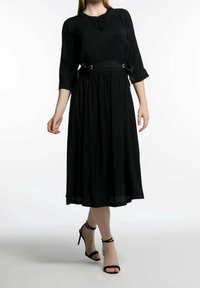 Svart midiklänning med rund halsringning, trekvartsärmar och sidoknytningar med metalliska detaljer, tillverkad av lättviktsmaterial.