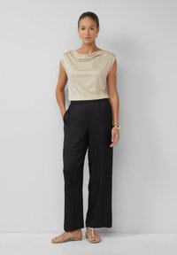 Beige satijnen top met gedrapeerde halslijn, gecombineerd met zwarte wijde broek. Accessoires zijn onder andere een gouden armband en zilveren sandaaltjes met bandjes.