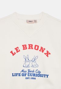 Sweatshirt de cor creme com texto vermelho e azul "LE BRONX" e "LIFE OF CURIOSITY", com uma ilustração de dois coelhos.