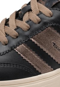 Gros plan d'une basket noire et marron avec des lacets beige et une texture en cuir et tissu.