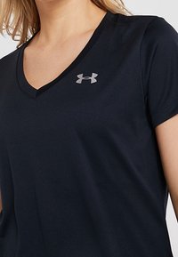 Zwarte v-hals t-shirt van gladde stof met een klein zilveren logo op de linkerborst en korte mouwen.