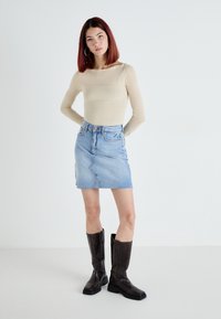 Beige long-sleeve top paired with a light blue denim mini skirt. Model wears knee-high black leather boots with square toes. Plain background.