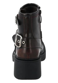 Botín de cuero marrón con un acento de hebilla plateada, suela negra texturizada y puntera redonda con un cuello acolchado.