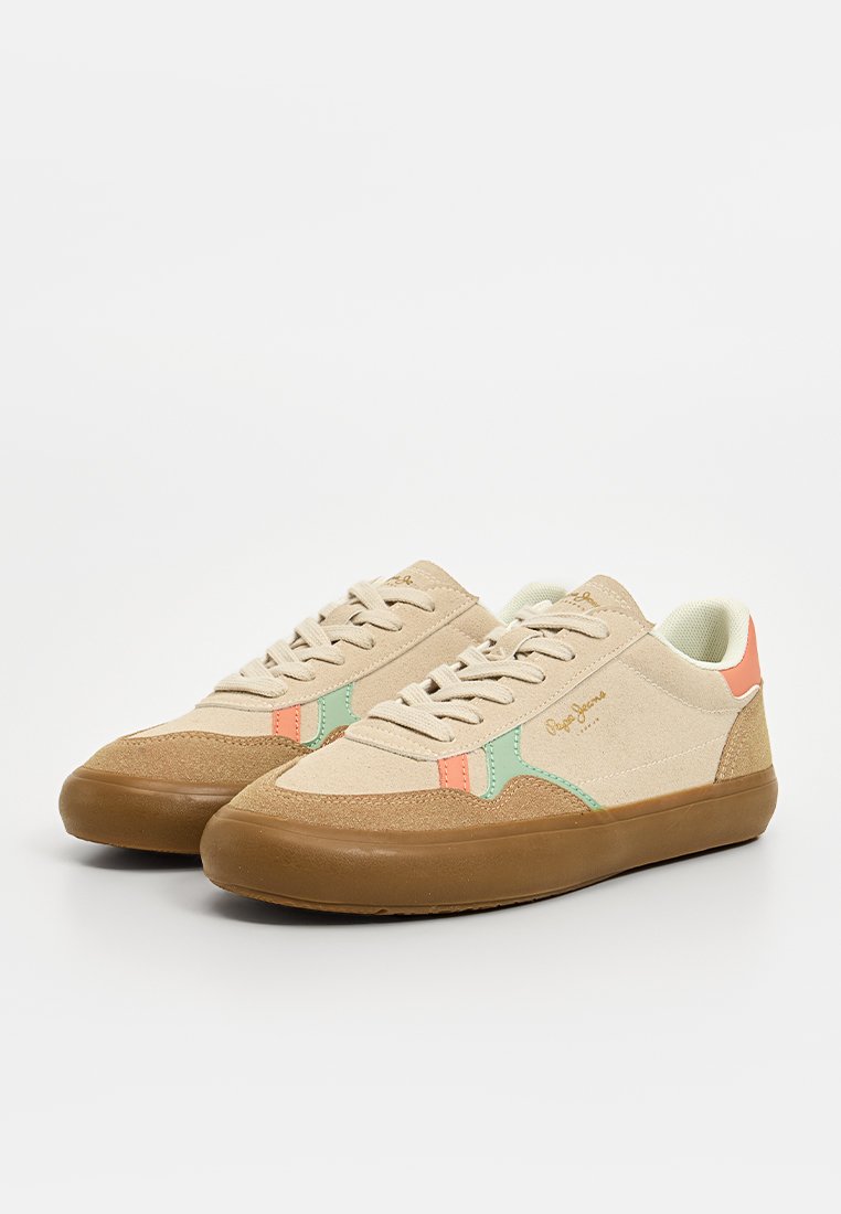 Zapatillas beige con parte superior de lona texturizada, acentos en verde y coral, suela de goma marrón y cordones blancos. Presenta un diseño de punta redondeada.