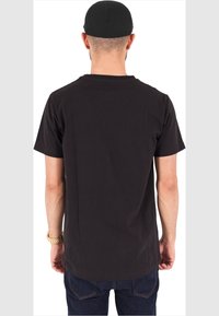 Black cotton t-shirt with short sleeves, straight cut, and rounded neckline. Visible stitching and smooth texture. Worn with dark denim jeans.