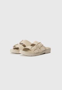 Beige sandaler med dobbel justerbar stroppdesign, mykt semsket materiale, tykk gummisåle for grep, og åpen tå-stil.