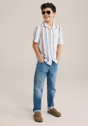 Chemise à manches courtes rayée en blanc, bleu pastel et rouge avec une poche sur la poitrine, associée à un jean bleu moyen retroussé et des mocassins marron.