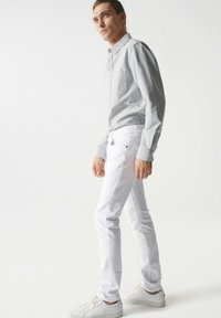 Jasnoszara, długorękawowa koszula zapinana na guziki z kieszenią na piersi, w połączeniu z białymi slim-fit dżinsami i białymi sneakersami. Prosty design i gładka tekstura.