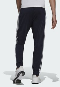 Marineblaue Sporthosen mit weißen Seitenstreifen, schmaler Schnitt, gerippter Bund und weicher Stoffqualität, kombiniert mit weißen Sportschuhen.