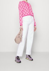 Różowy krótki sweter z białym wzorem w serca, białe wysokie spodnie jeansowe, jasnofioletowe trampki oraz beżowa torba zawiązana na supeł.